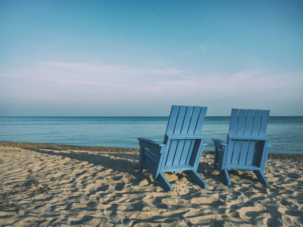 Deux chaises bleu sur une plage devant un lac