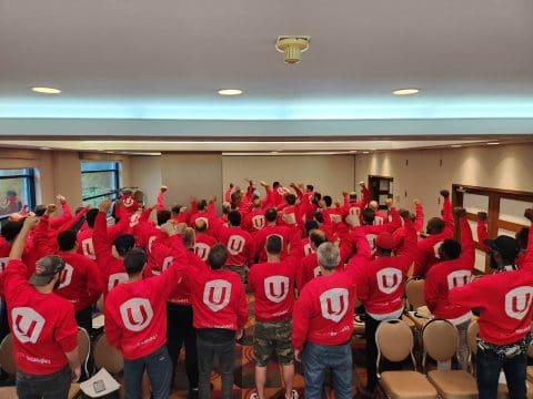 Plusieurs personnes de dos, le poing dans les airs arborant leur chandail d'unifor rouge